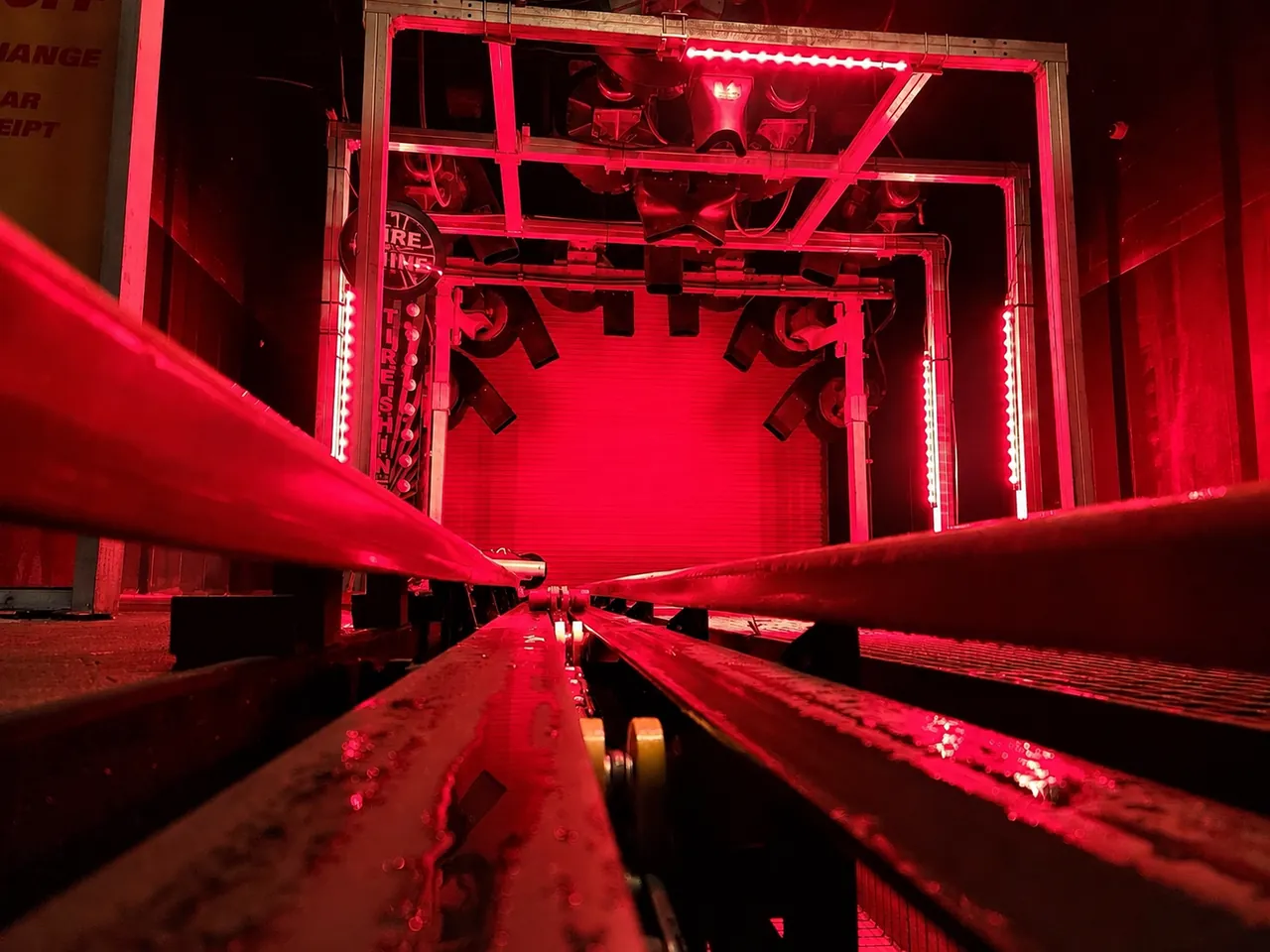 Car wash conveyor rails and rollers inside a red-lit tunnel